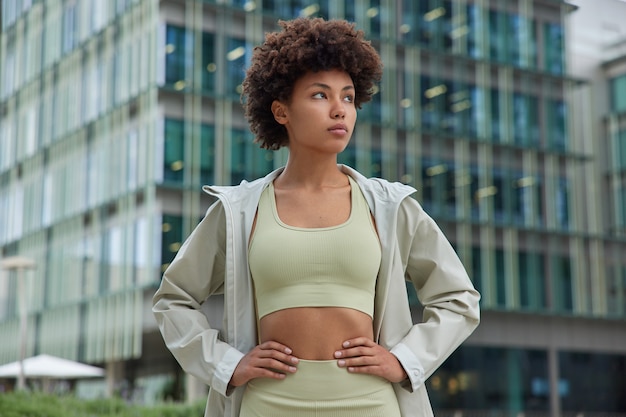 une femme en bonne forme physique car les trains gardent régulièrement les mains sur la taille vêtue d'un survêtement profite d'un entraînement matinal actif en milieu urbain