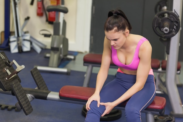 Femme en bonne santé avec un genou blessé, assis dans la salle de gym