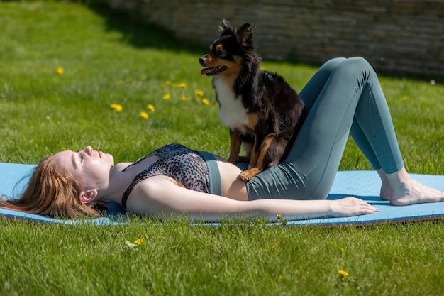 Une femme en bonne santé jouant avec un chiot assis sur un tapis de yoga