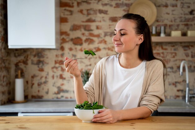 Une femme en bonne santé mange une salade délicieuse et saine dans un bol à sa table à manger