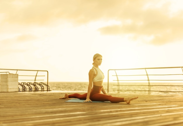 Femme en bonne santé pratiquant le yoga sur la promenade du bord de mer. Femme sportive pratiquant la ficelle au lever du soleil