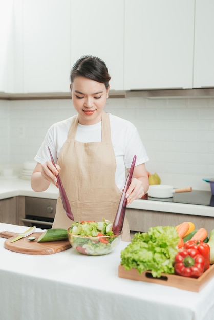 Une femme en bonne santé prépare une salade de légumes frais avec de la tomate et de la salade à l'huile d'olive