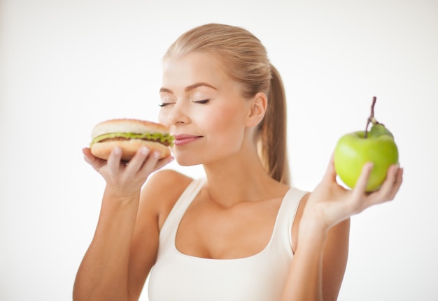 femme en bonne santé sentant un hamburger et tenant une pomme