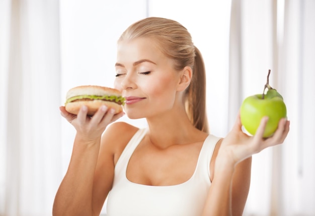 femme en bonne santé sentant un hamburger et tenant une pomme