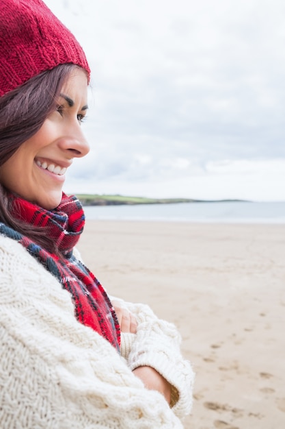 Femme en bonnet et pull souriant à la plage