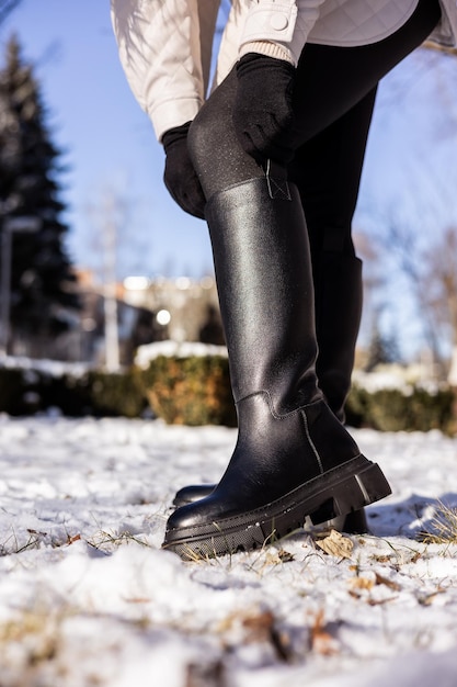 Femme en bottes noires à la mode sur la neige blanche gros plan Jambes de femmes dans des bottes en cuir d'hiver élégantes