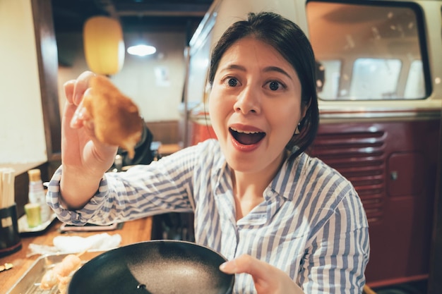 femme avec la bouche grande ouverte montrant le partage d'une délicieuse collation japonaise kushiage à la caméra. fille ayant une brochette de style japonais dans un repas de fin de soirée au comptoir de bar assis izakaya. femme heureuse nourrir son petit ami