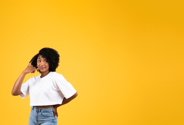 Femme bouclée afro-américaine souriante et confiante du millénaire en t-shirt blanc montre le signe de la main d'appel