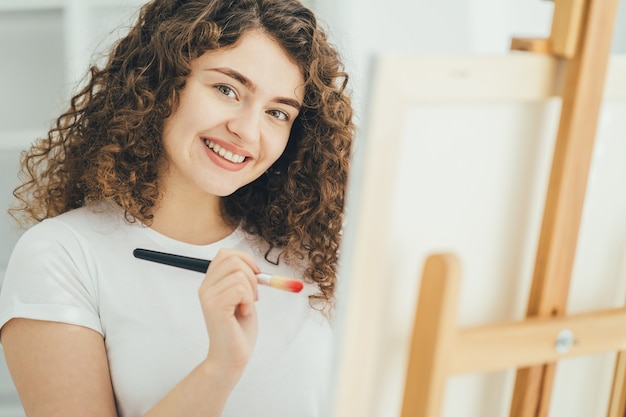 La femme bouclée avec un pinceau d'art peignant une image sur le chevalet