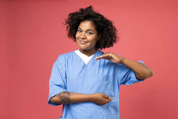 Photo femme bouclée souriante en vêtements de médecin sur fond rose