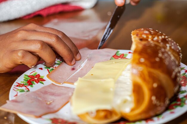 Photo une femme boulanger coupe du jambon pour préparer un sandwich avec du fromage et de la mayonnaise pour le petit déjeuner sur une assiette sur une table