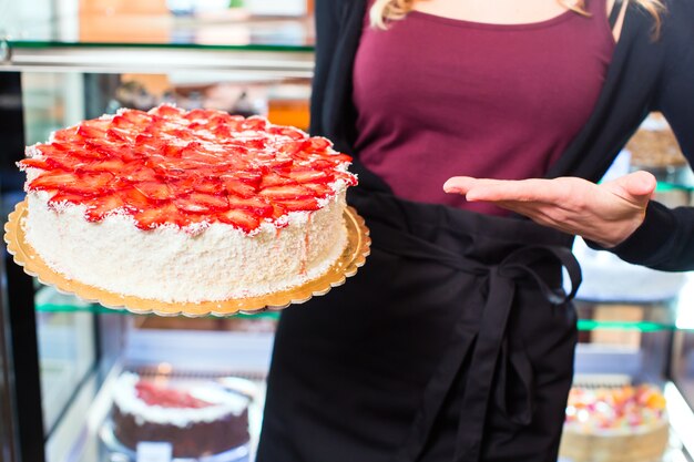 Femme boulanger présentant un gâteau dans une confiserie