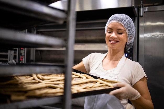 Femme boulangère debout près du plateau en métal et préparant la pâte crue pour la cuisson