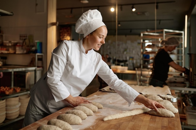 Femme boulangère formant des pains à partir de pâte crue dans une cuisine professionnelle