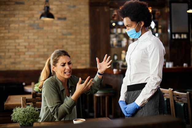 Femme bouleversée ayant une dispute avec une serveuse afro-américaine dans un café