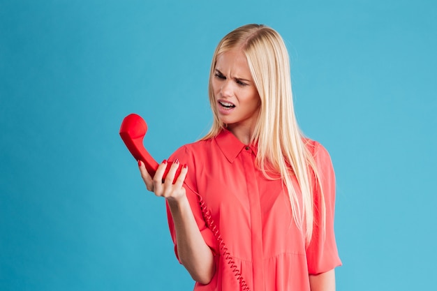 Femme bouleversée en colère criant sur le tube du téléphone isolé sur un mur bleu