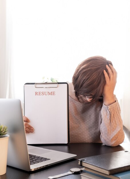 Une femme bouleversée a fermé votre visage de mains près de son lieu de travail avec un ordinateur portable et une application de reprise.