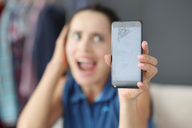 Femme bouleversée tenant un smartphone cassé dans les mains, choc causé par les dommages causés au concept de téléphone