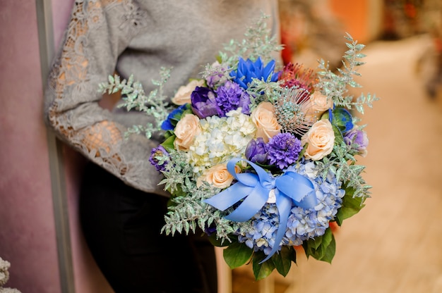 Femme avec un bouquet d'hortensias bleus et blancs, de roses beiges et de plantes succulentes