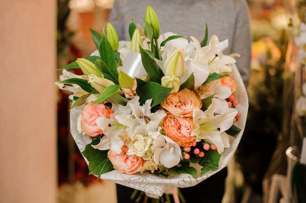 Femme avec un bouquet de lys, orchidées, roses en forme de pion dans du papier d'emballage