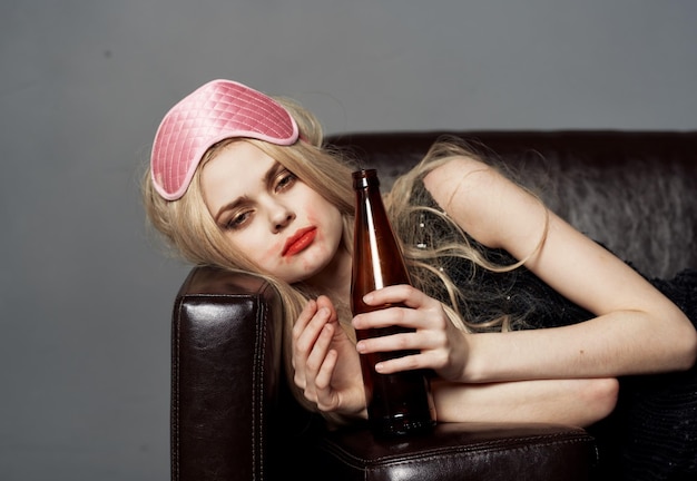Femme avec une bouteille de bière sur le canapé masque de sommeil de dépendance à l'alcool sur la tête