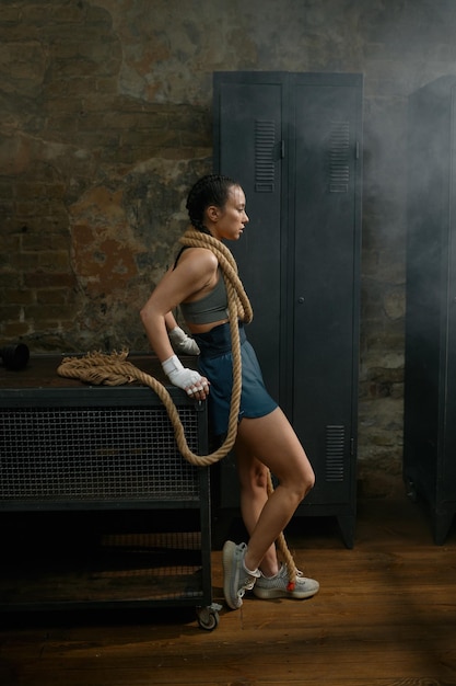 Une femme boxeuse magnifique enroulée dans une corde sur le fond d'un gymnase.