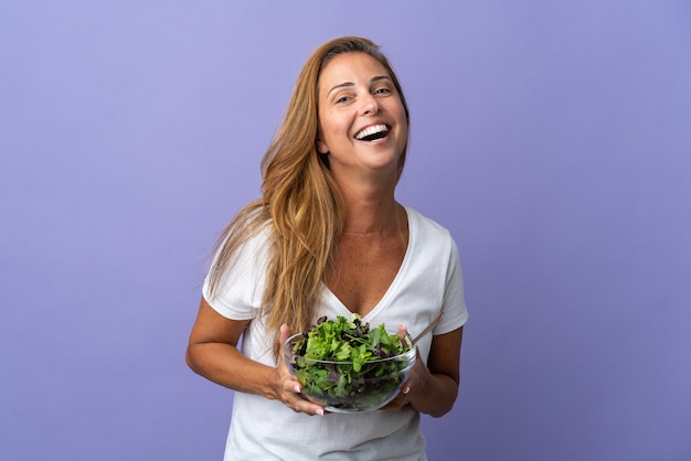 Femme brésilienne d'âge moyen isolée sur violet tenant un bol de salade avec une expression heureuse