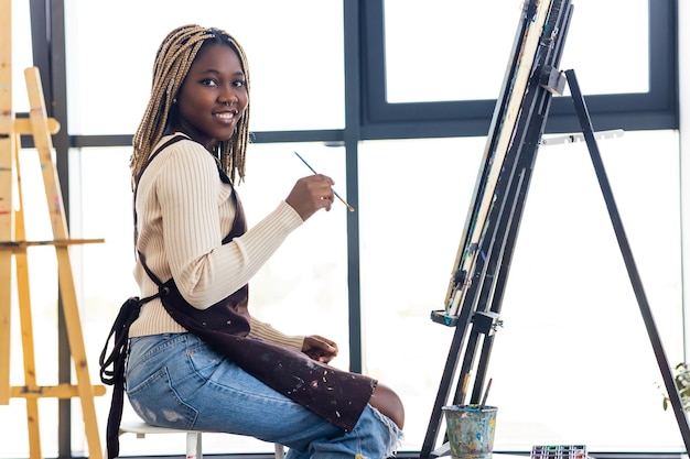 Femme brésilienne avec des dreadlocks en blouse blanche dans un studio d'art