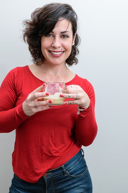 Femme brésilienne avec un grand sourire sur son visage, regardant la caméra et tenant une tasse de cappuccino.