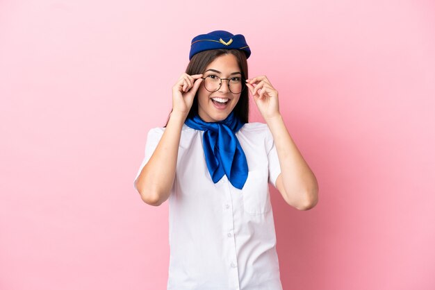 Femme brésilienne d'hôtesse d'avion isolée sur fond rose avec des lunettes et surprise