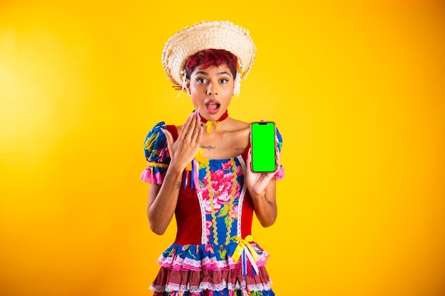 Femme brésilienne avec des vêtements festa junina Arraial Fête de Saint John montrant un smartphone avec écran vert