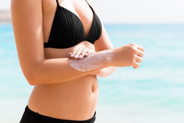 Femme bronzée applique un écran solaire sur sa main à la plage