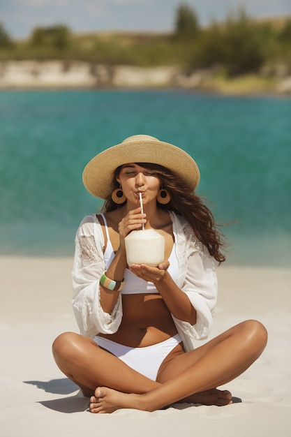 Femme bronzée en bikini avec noix de coco sur la plage