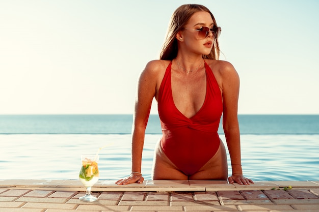 Femme bronzée en bikini rouge dans une piscine avec cocktail