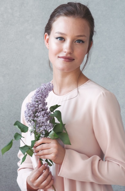 Femme avec brunch lilas sur fond gris. Prise de vue en studio.