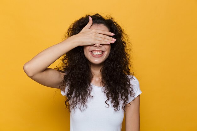 femme brune 20s aux cheveux bouclés souriant et yeux coniques avec palm isolé sur jaune