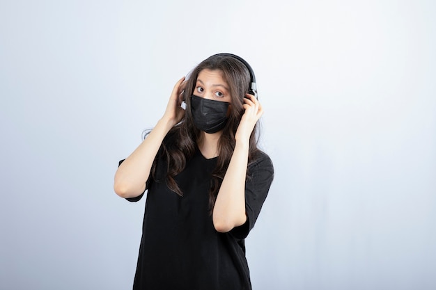 Femme brune aux cheveux longs dans un masque médical portant des écouteurs.