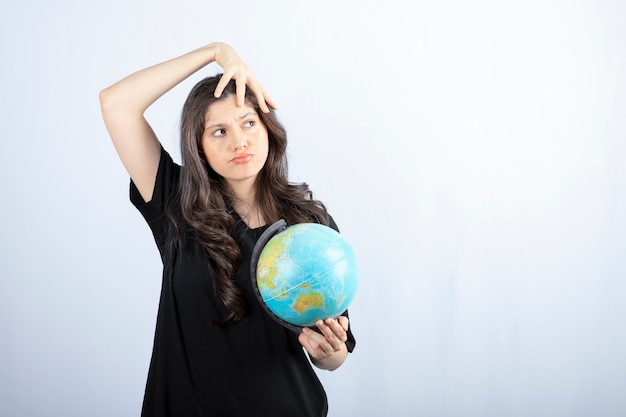 Femme brune aux cheveux longs tenant le globe terrestre et posant.