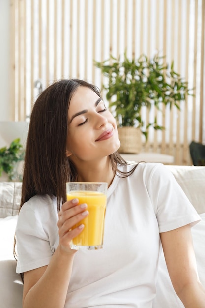 Femme brune aux yeux fermés tenant un verre avec du jus d'orange