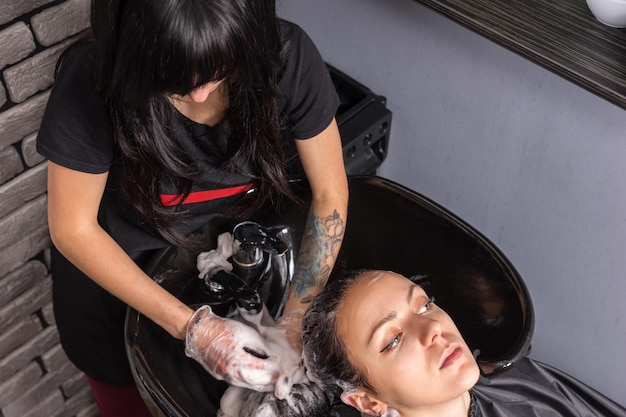 Femme brune ayant les cheveux lavés et savonnés par une styliste féminine dans un lavabo dans un salon de beauté