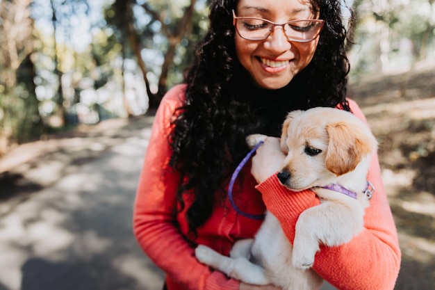 Femme brune bouclée latine, embrassant et tenant avec un chiot golden retriever dans le parc.