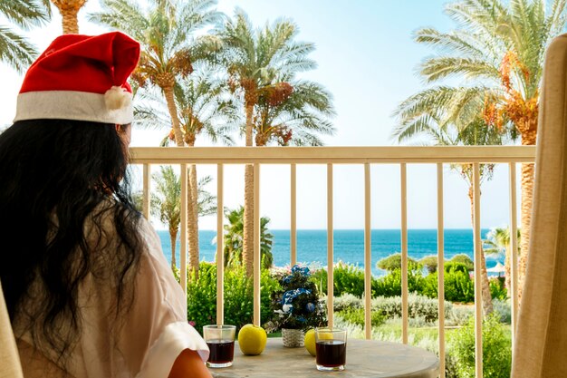 Femme brune en chapeaux de père Noël fête Noël sur le balcon à une table