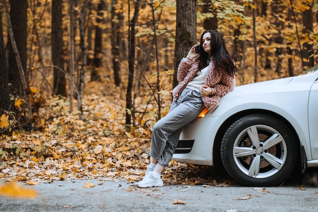 Femme brune confiante debout près de la voiture et appeler le téléphone en préparant votre voiture pour l'automne automne