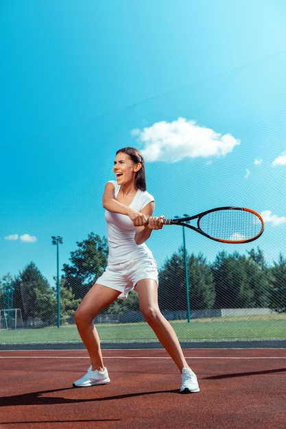 Femme brune criant en frappant la balle de tennis