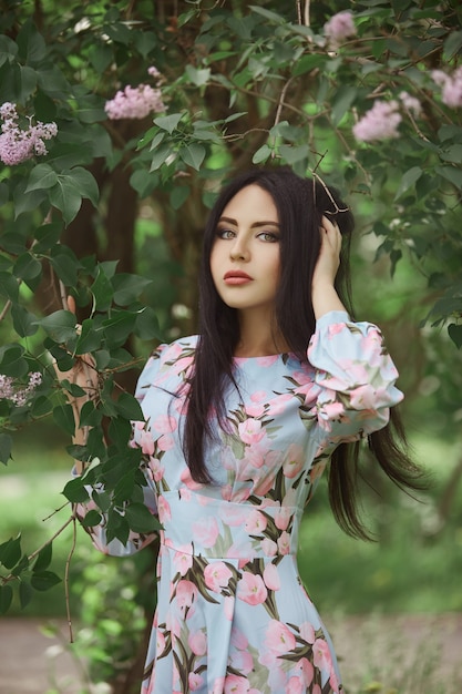 Femme brune dans les branches d'un bel arbre en fleurs. Robe d'été courte sur le corps de la fille. Promenade printanière dans le parc, ambiance romantique