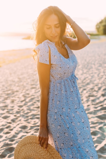 femme brune dans une élégante tenue d'été et un chapeau de paille dans les rayons du soleil sur une promenade dans la nature