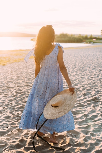 femme brune dans une élégante tenue d'été et un chapeau de paille dans les rayons du soleil sur une promenade dans la nature