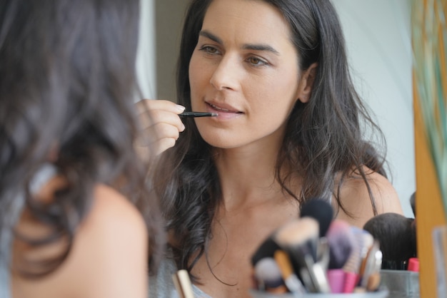 Femme brune devant un miroir appliquant une lipstik