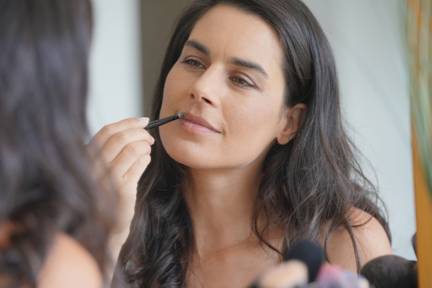 Femme brune devant un miroir appliquant une lipstik