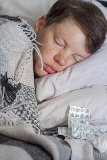 Femme brune dormant dans son lit sous une couverture à carreaux avec des pilules